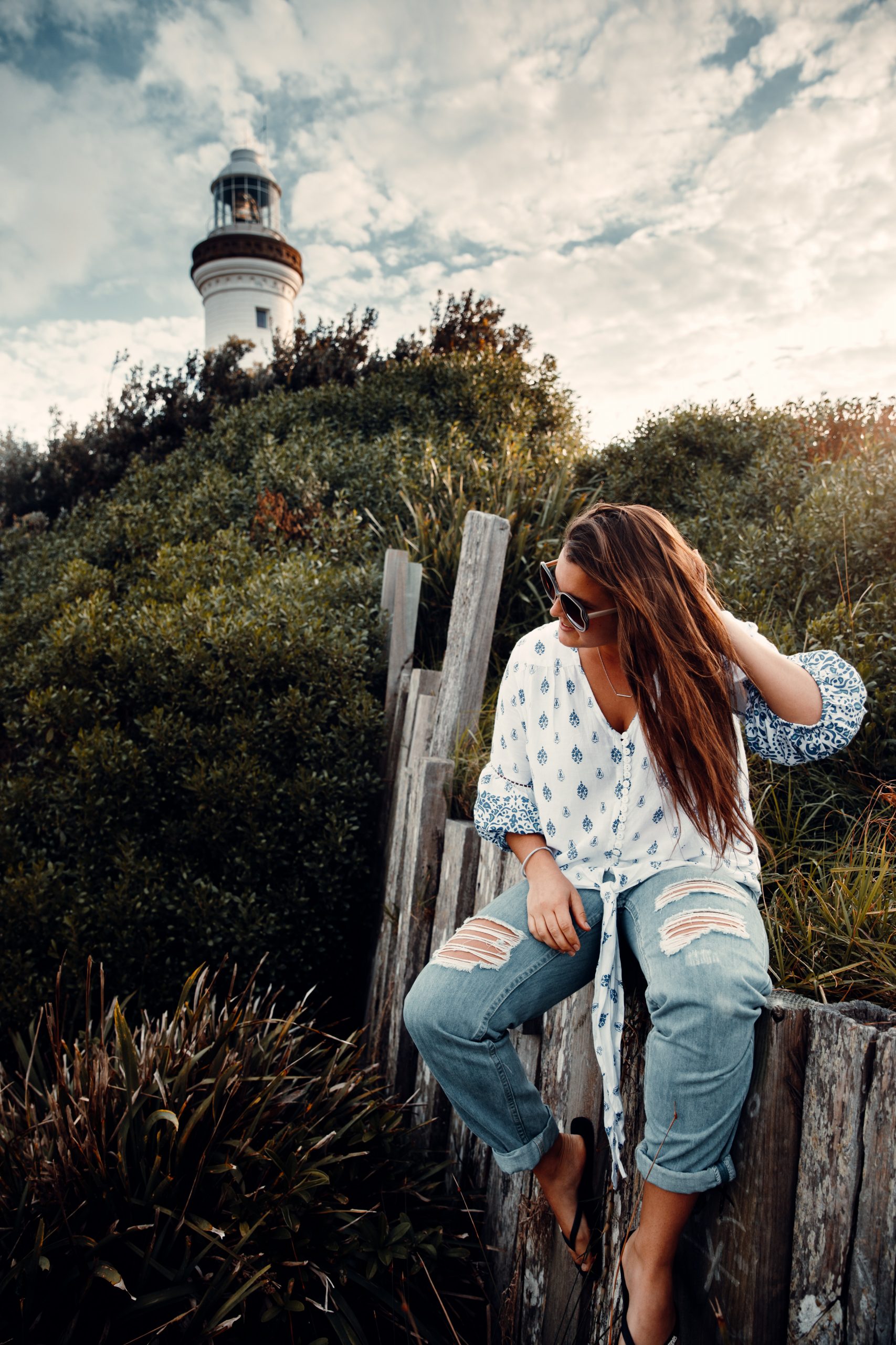 woman sitting on fence in front of Norah head lighthouse looking out at the beach and ocean